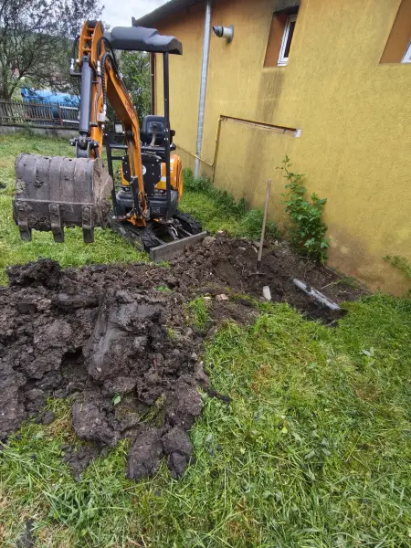 A kotró a ház fala mellett halad a nyomvonalon.